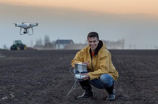 Drone pilot on a dirt field with a drone in the background.